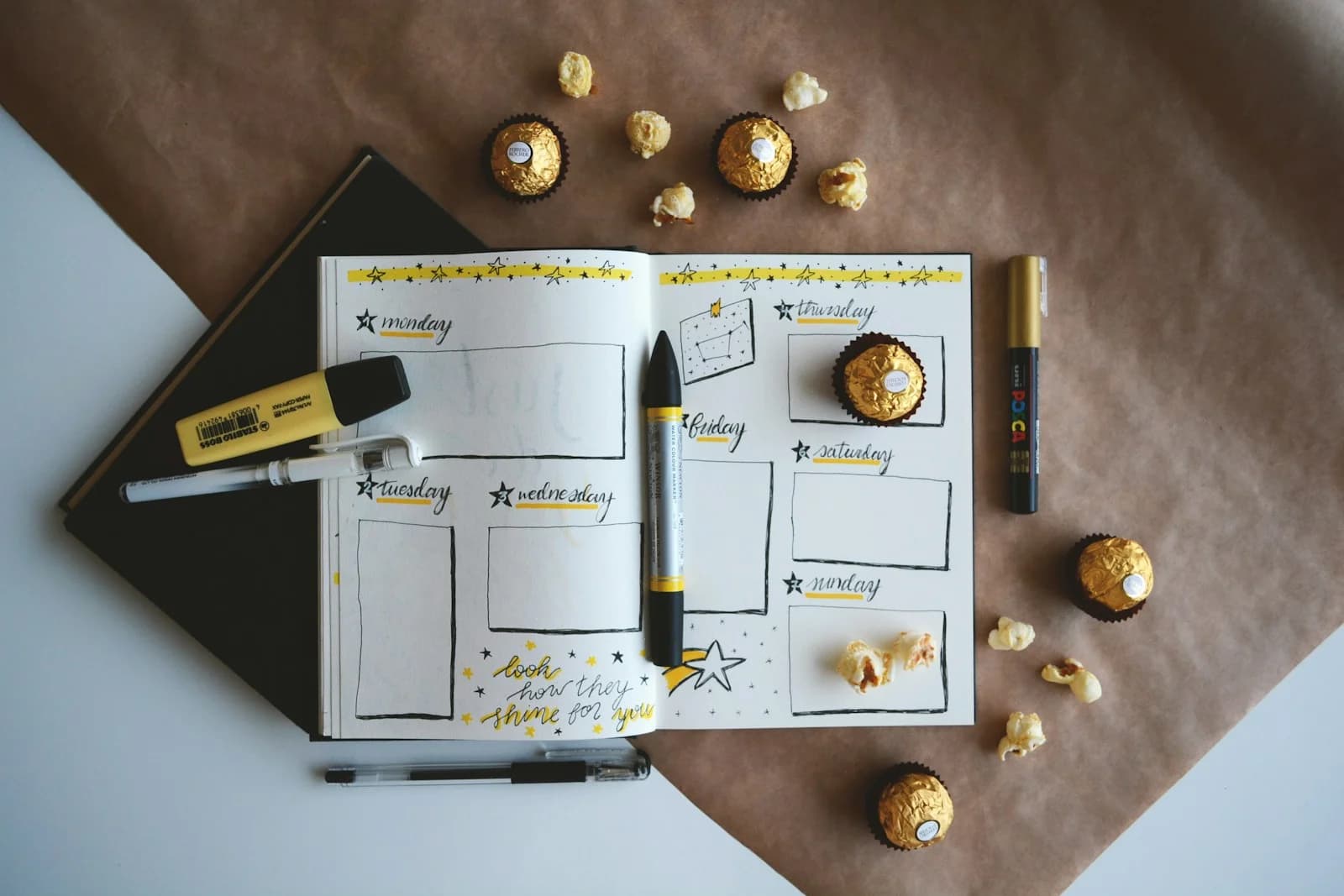 An open weekly planner with pens and small wrapped chocolates on a desk.